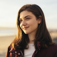 a young woman in a burgundy jacket standing on the beach