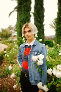 a young man in a denim jacket standing in a garden