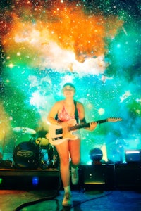 a woman playing a guitar in front of a colorful background
