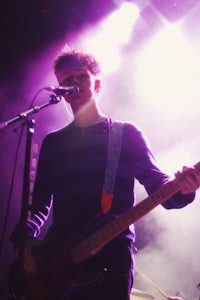 a young man playing a bass in front of a microphone