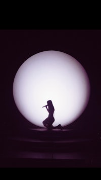 a silhouette of a woman on stage in front of an oval light