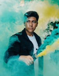 a young man holding a blue and green smoke