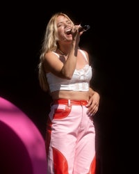 a woman in a white top and pink pants singing into a microphone