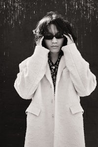 a black and white photo of a woman wearing a coat and sunglasses