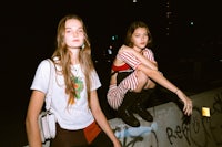 two girls sitting on a wall with graffiti on it