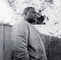 a black and white photo of a man standing in front of a fence