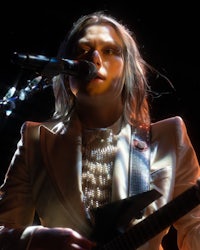 a woman in a white suit playing an electric guitar