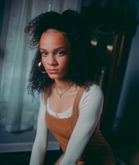 a young woman with curly hair sitting in front of a window