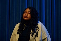 a woman with dreadlocks standing in front of a blue curtain