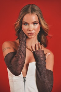 a woman in a white top and brown gloves posing on a red background