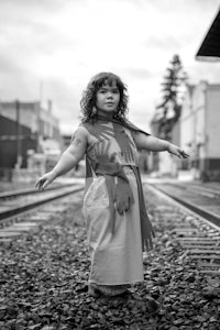 a little girl in a costume standing on railroad tracks