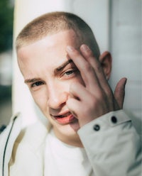 a man with a shaved head leaning against a wall