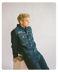 a young man in a denim jacket leaning on a wooden box