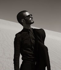 a man in black and white standing on a sand dune