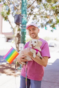 a man in a pink shirt holding a dog with a rainbow flag