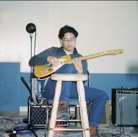 a man sitting on a stool playing an electric guitar