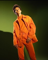a man in an orange jacket posing in front of a green background