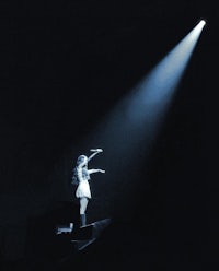 a woman in a white dress standing on a stage in front of a spotlight