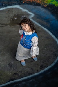 a girl in a blue dress standing in front of a colorful mural