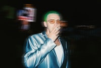 a man with green hair smoking a cigarette in a city