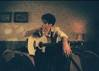 a man sitting on a bed with an acoustic guitar