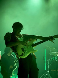 a man playing a guitar on stage in front of green lights