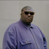 a man in a purple shirt and sunglasses is standing in front of a wall