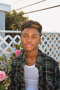 a young man in a plaid shirt standing in front of roses