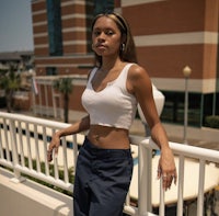 a young woman standing on a balcony wearing a white top and blue pants