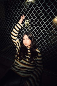 a woman in a striped sweater leaning against a fence