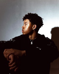 a young man sitting in front of a white wall