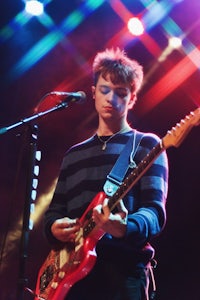 a young man playing an electric guitar in front of a microphone