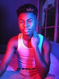 a young man in a tank top sitting on a bed